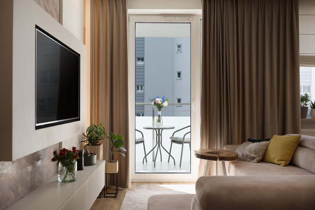 Wnętrze nowoczesnego salonu z widokiem na balkon, stół z kwiatami i rośliny doniczkowe