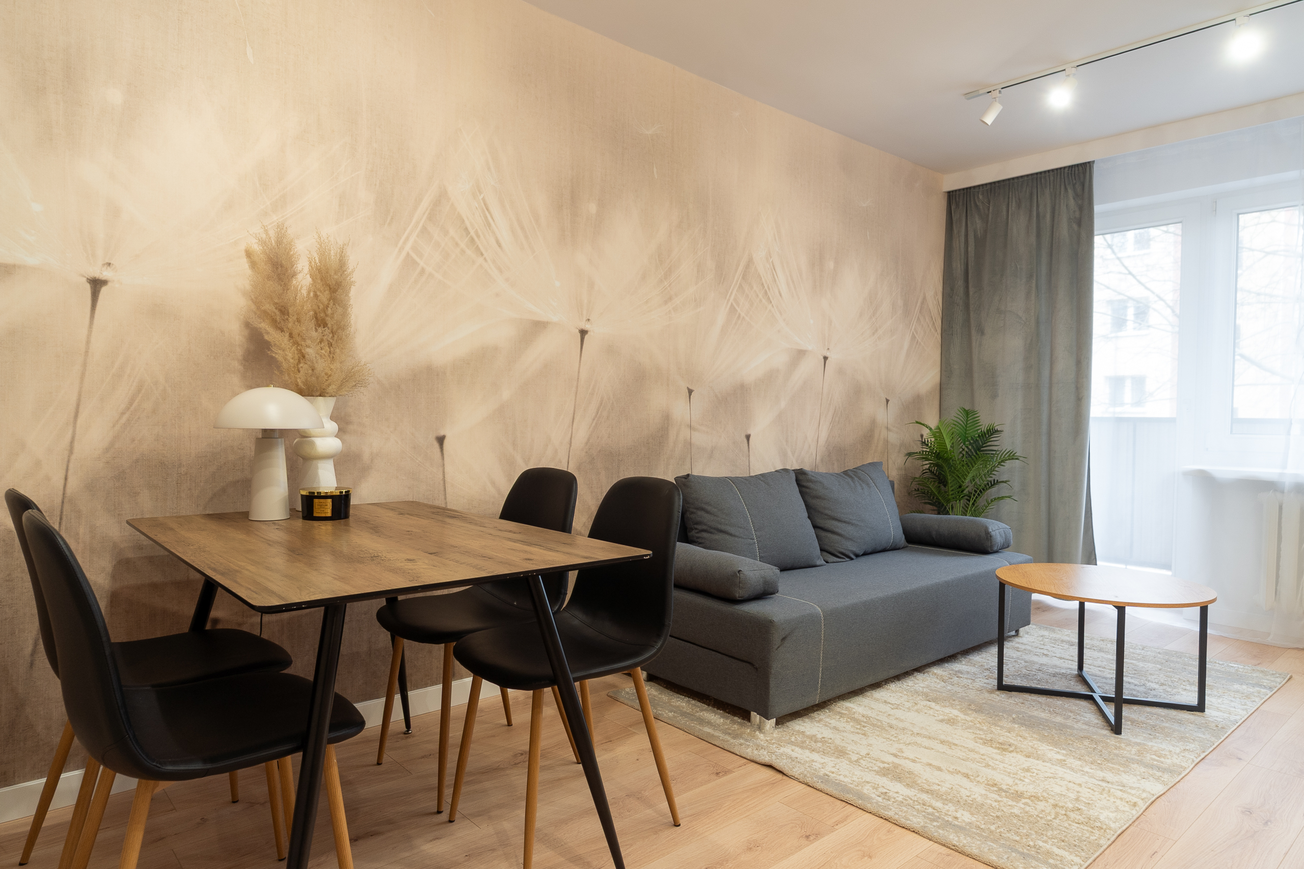 Przytulny salon z szaro-niebieską kanapą, drewnianym stołem i dekoracyjną tapetą.