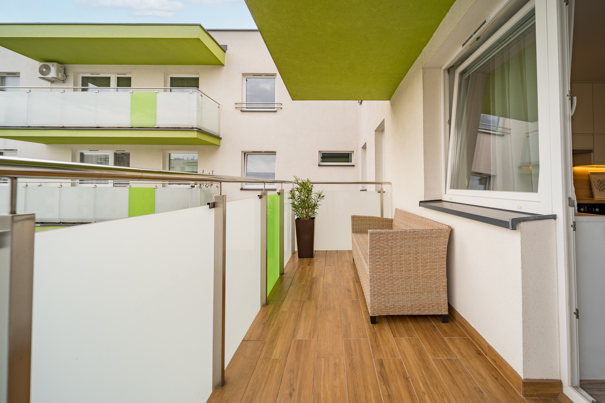 Balkon z drewnianą podłogą, sofą oraz rośliną w donicy