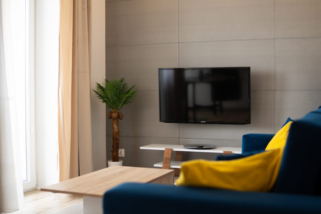 Stylowy salon z niebieską sofą, telewizorem na ścianie i rośliną