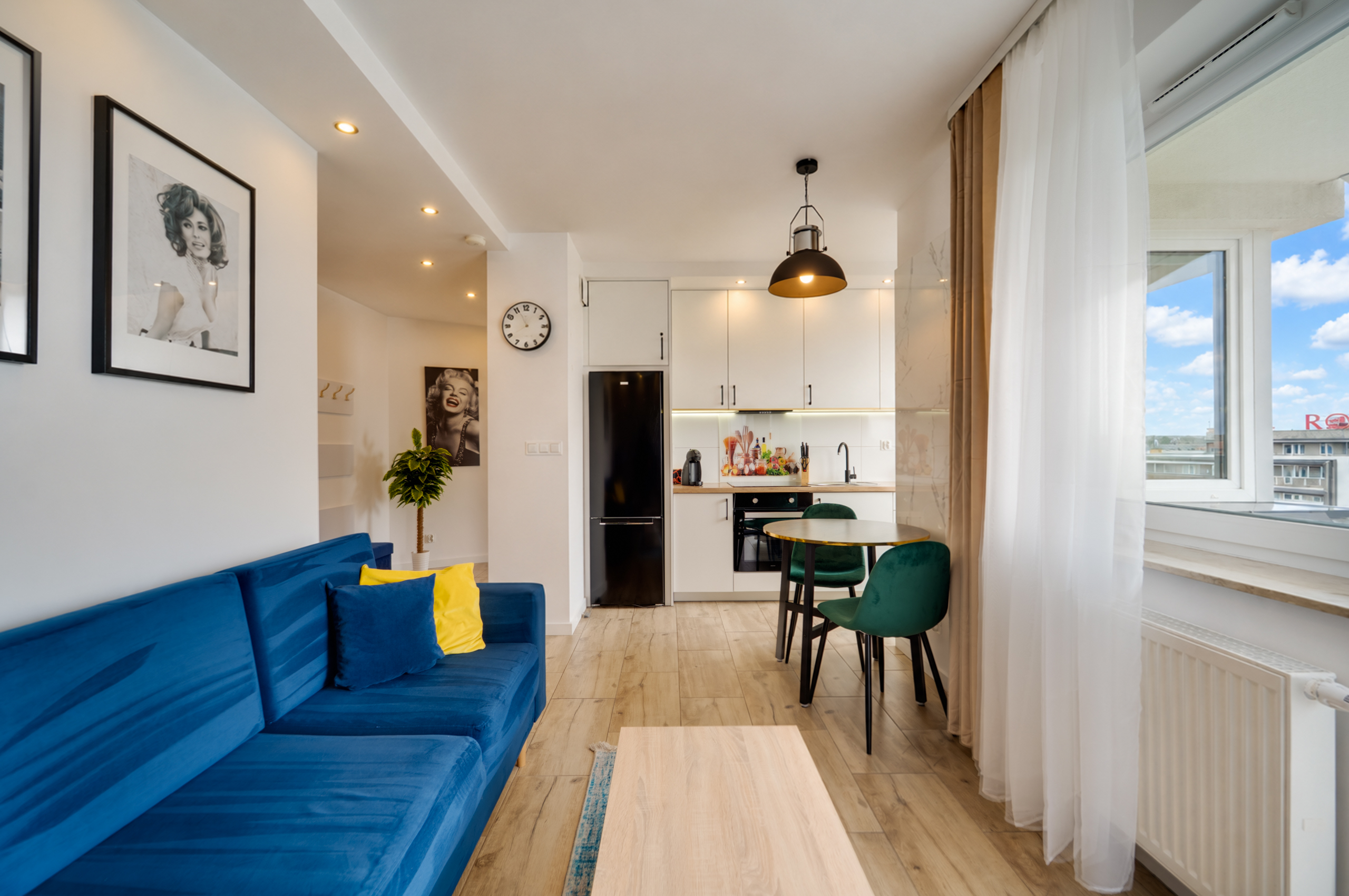 Nowoczesny salon z niebieską kanapą i zielonymi krzesłami, jasna kuchnia