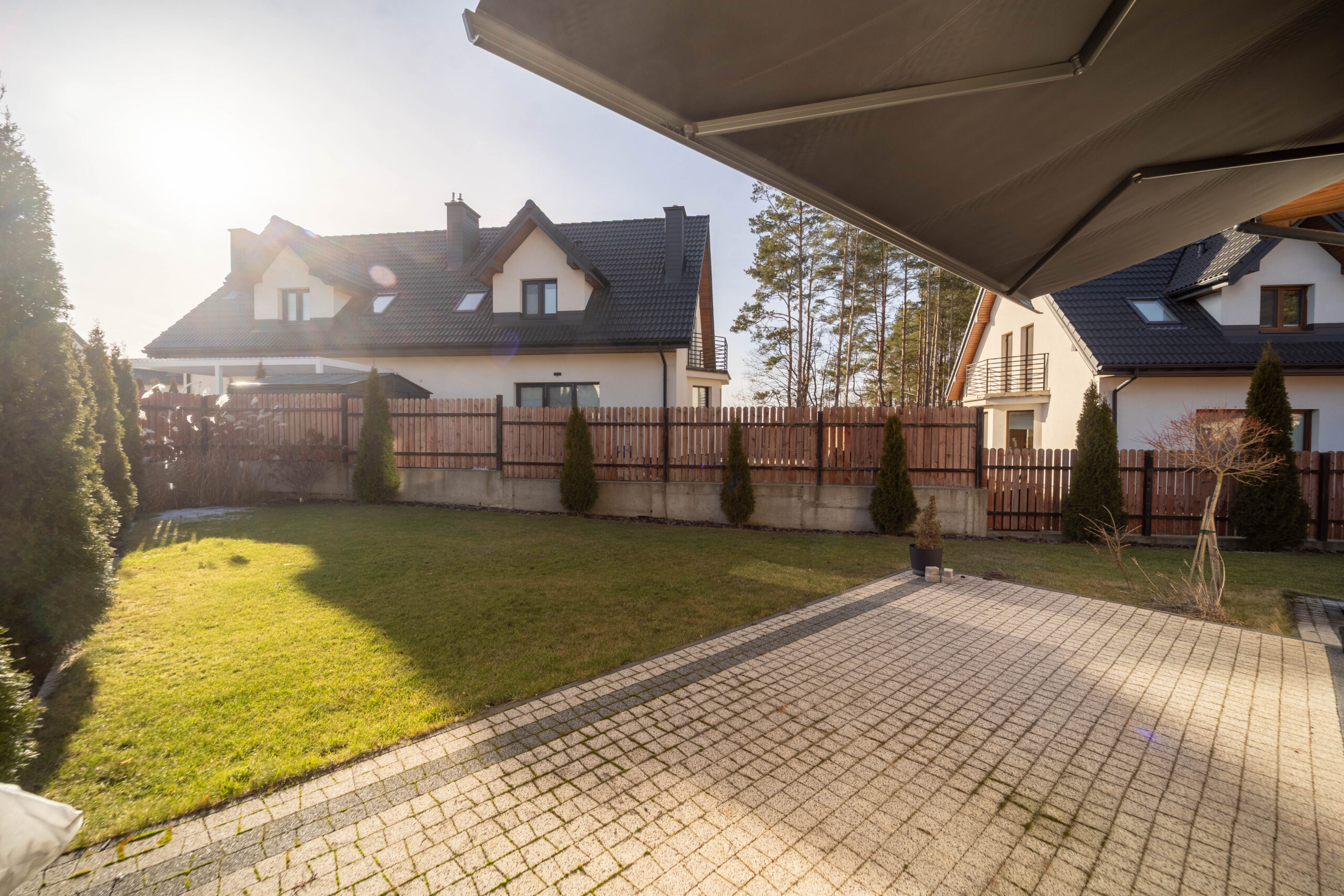 Zielony ogród z kostką brukową, w tle nowoczesny dom z dachem.